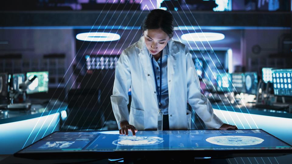Scientist in a lab coat interacts with a large touchscreen displaying digital data, surrounded by futuristic equipment and blue lighting.