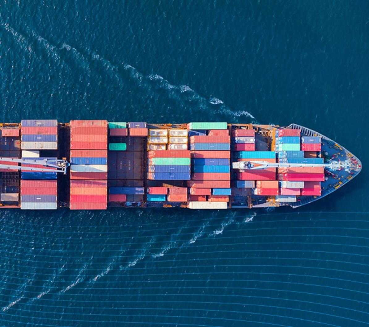 Aerial view of a colorful cargo ship loaded with containers, sailing on deep blue ocean waters, leaving a wake behind.