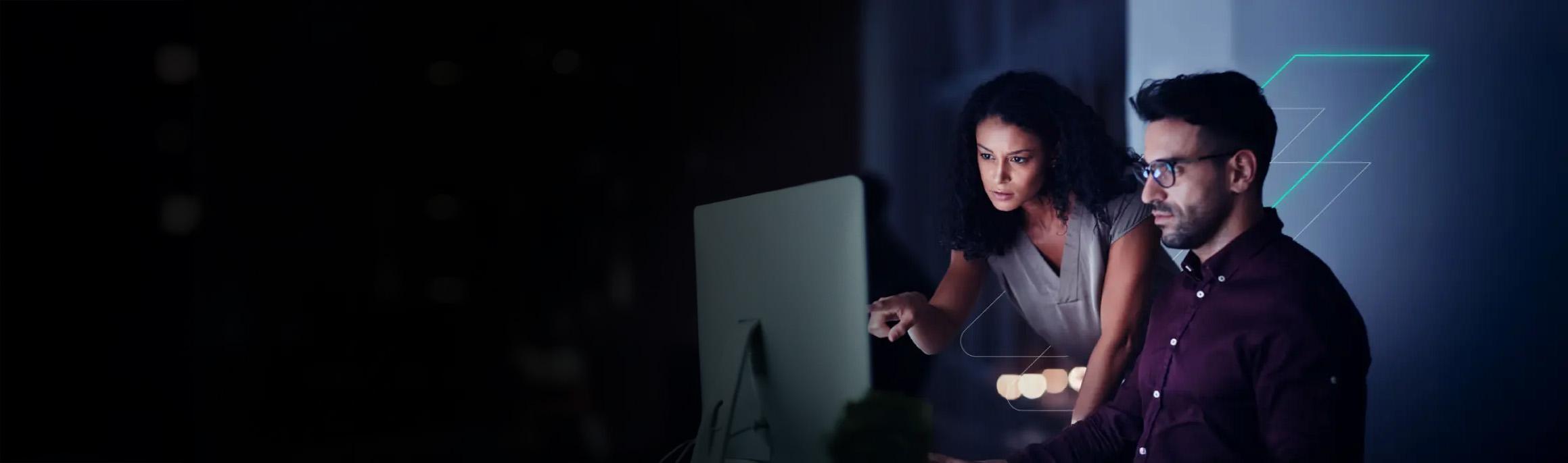 Two people focused on a computer screen in a dimly lit room, with abstract geometric shapes in the background.