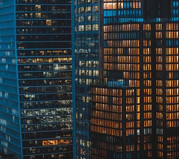 Close-up of modern skyscrapers at dusk, with glass facades reflecting warm lights, highlighting the contrast between cool and warm tones.